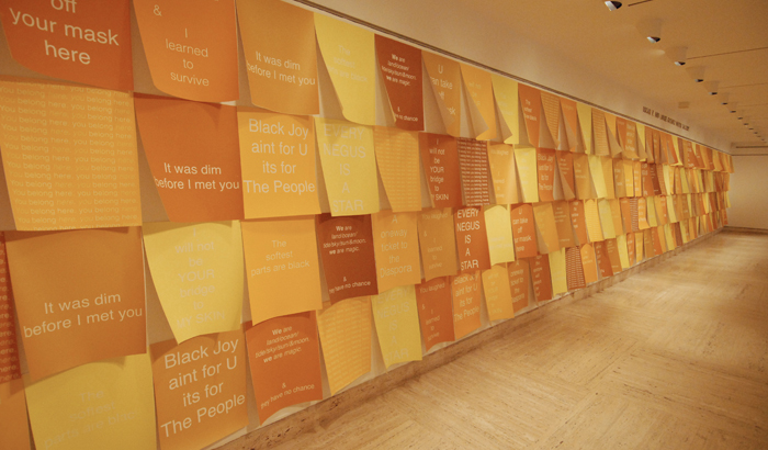Video still, orange sheets of paper lining a wall