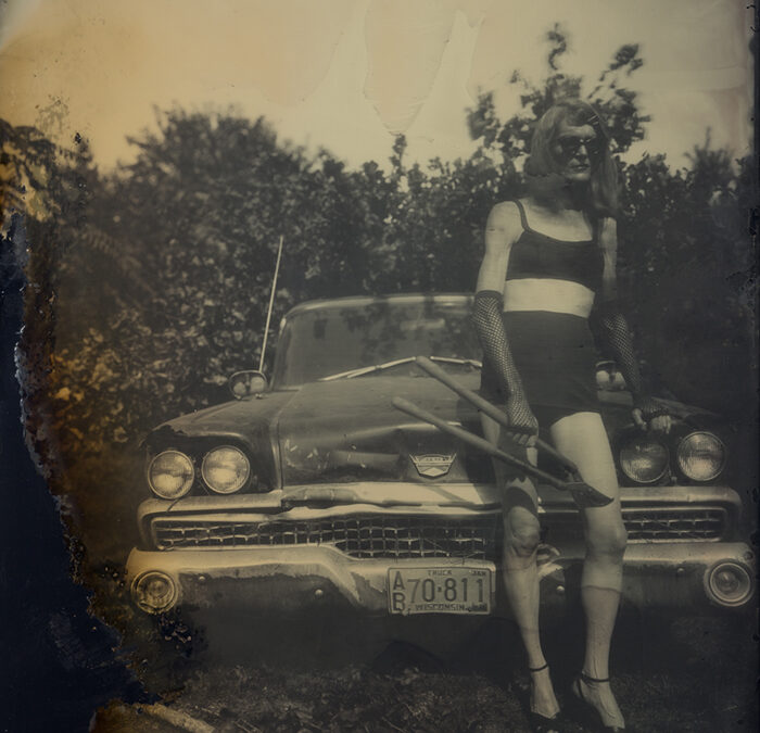 old cyanotype image depicting a woman standing with garden shears, clad in black bikini, in front of a vintage auto with Wisconsin plates.