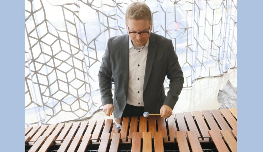 Sean Kleve is a white, adult man with blond hair and glasses playing the marimba