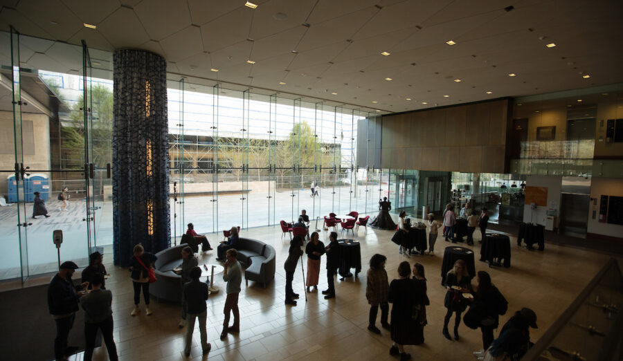 Approximately twenty people in the museum's lobby are silohuetted against the large windows