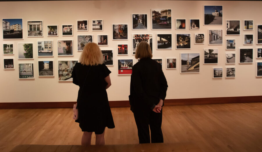 two figures seen from the back look at a wall hung with photographs