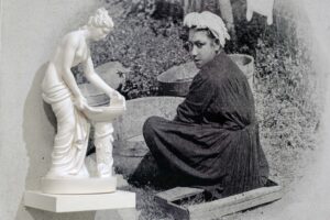 Black and white photo of a woman looking over her shoulder while seated, with a classical Western-style sculpture mounted to the photo