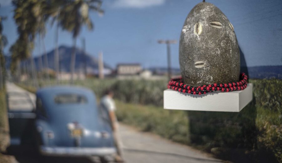 a photograph of a landscape with a road and a blue car, with a rock-like sculpture mounted on it