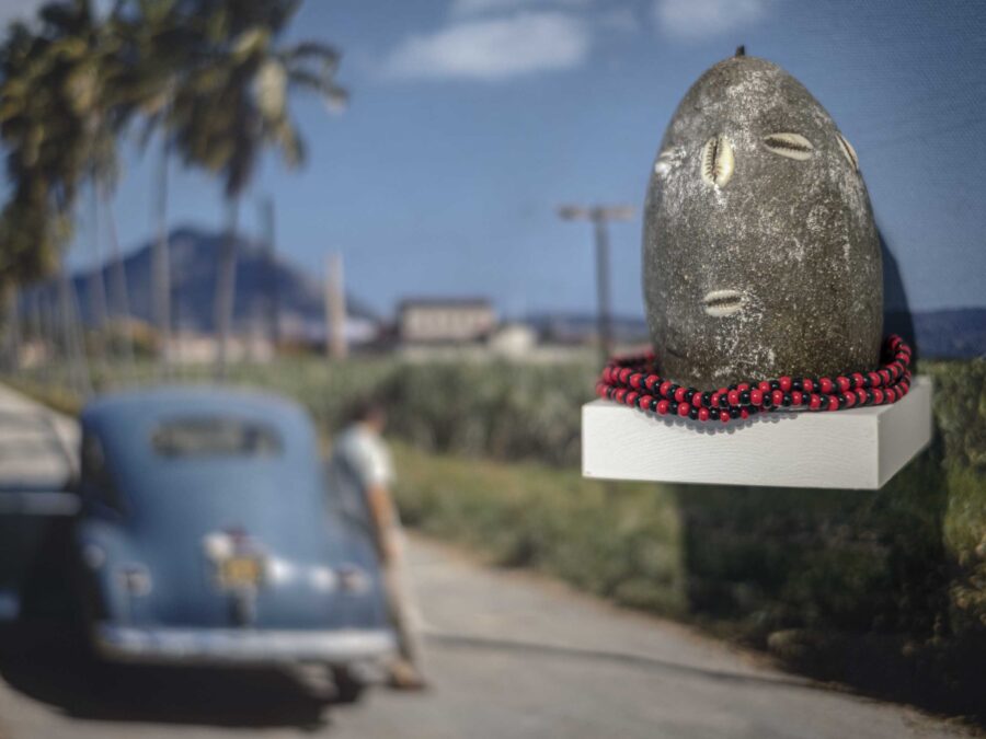 a photograph of a landscape with a road and a blue car, with a rock-like sculpture mounted on it