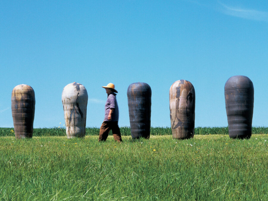 A green field, blue sky, with enormous ceramic vessels on the horizon. The artist, who is about the same height as the works, walks in front of them