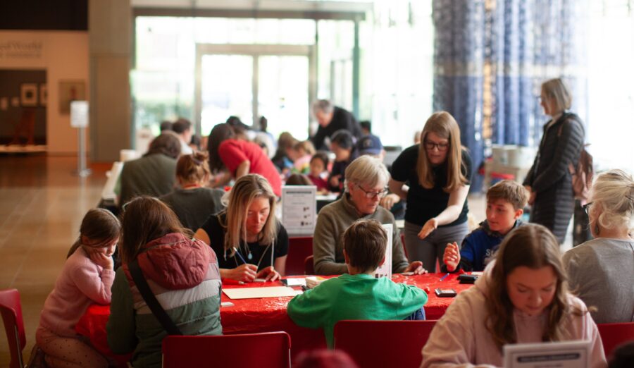 A variety of people seated at banquet tables doing crafts in the Mead Witter Lobby at the Chazen