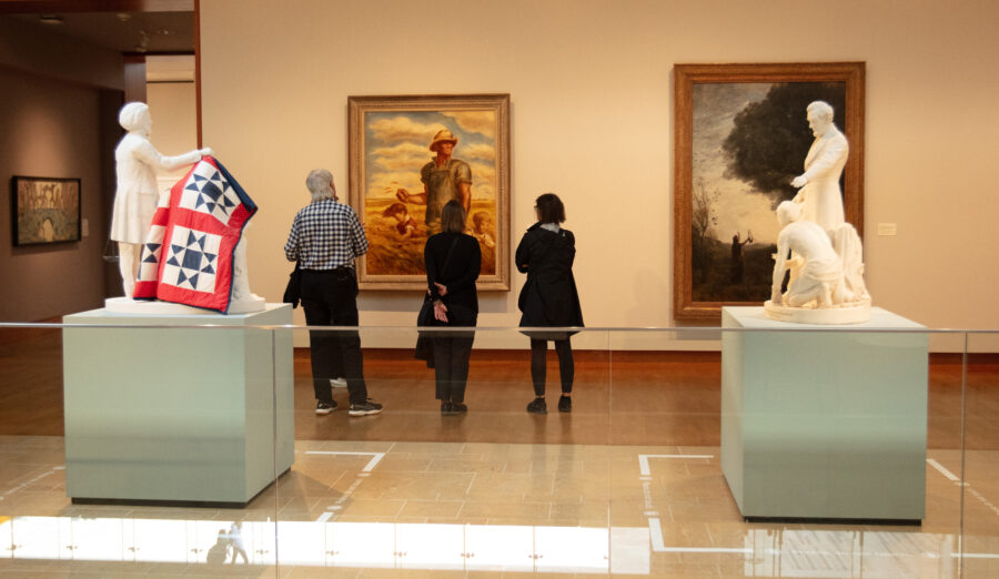 People on a museaum tour looking at painintgs with sculptures in the foreground.