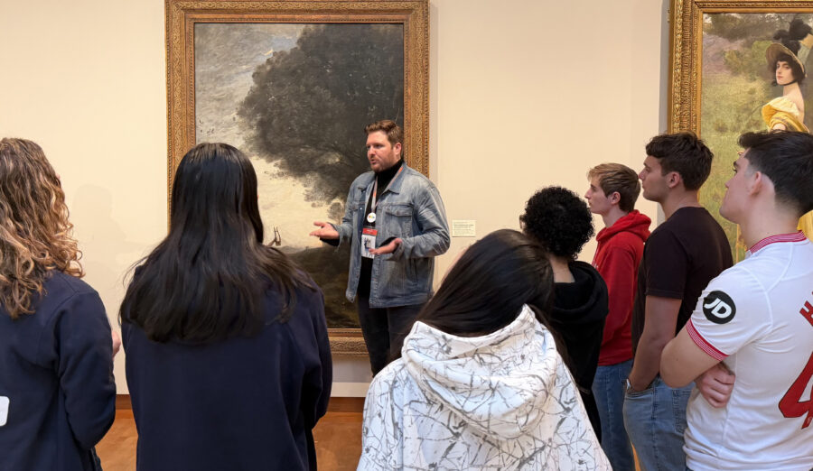 A tour group with a tall guide looks at a painting